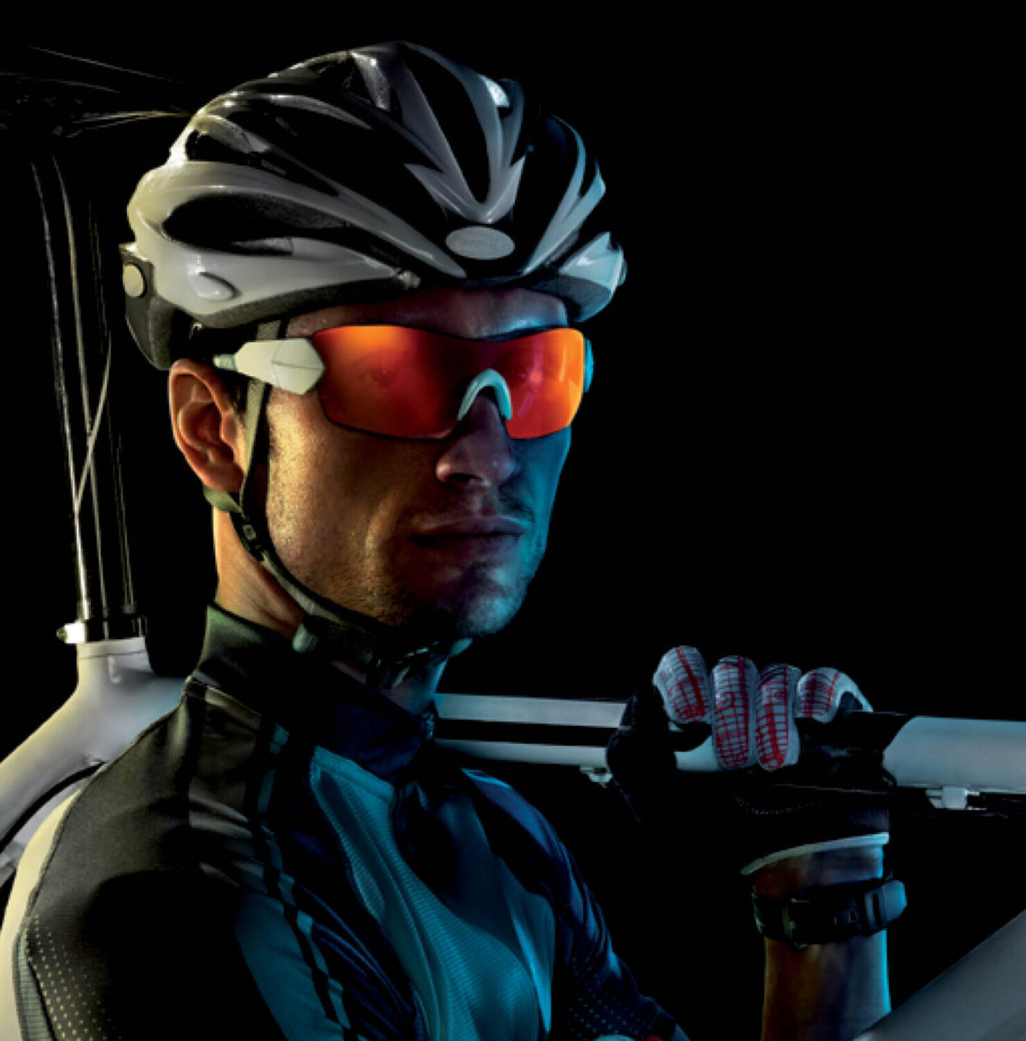 Cyclist with helmet and white bike wears red revex sports sunglasses against a black background.