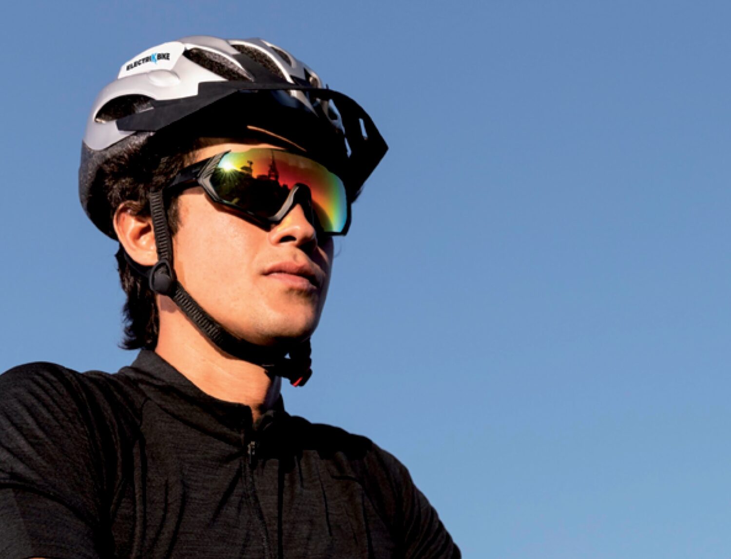 Cyclist wearing silver bicycle helmet and reflective sports glasses against a bright blue sky.