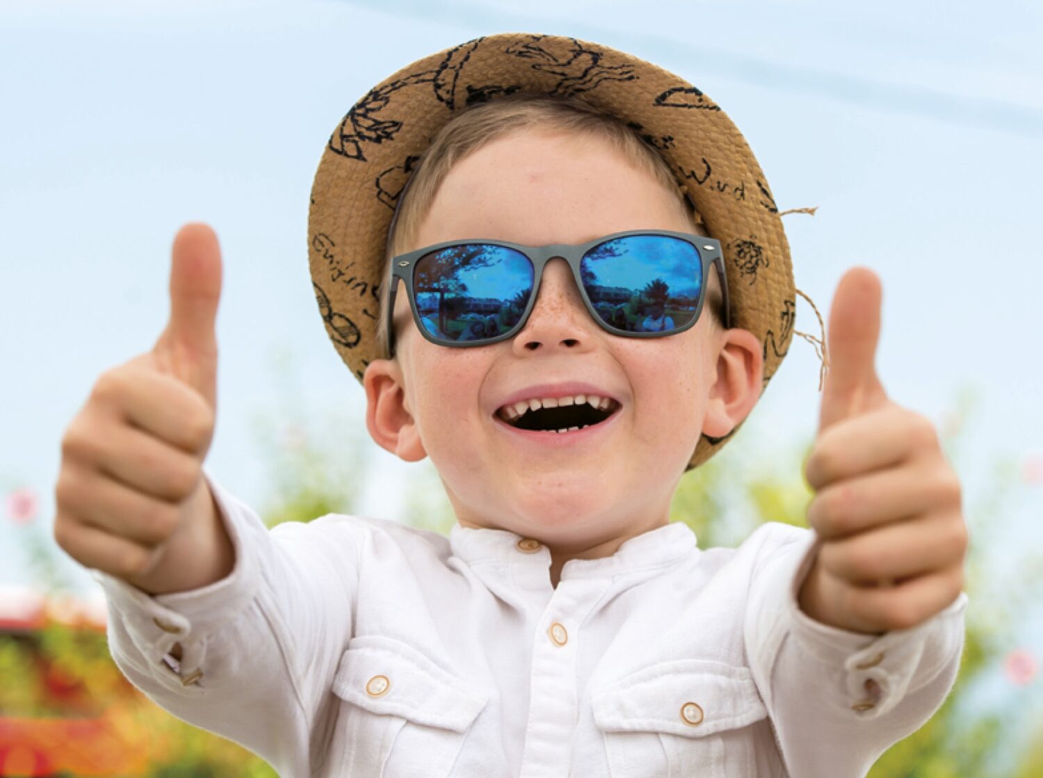 rosy-cheeked boy in a straw hat and blue children's sunglasses giving his thumbs up