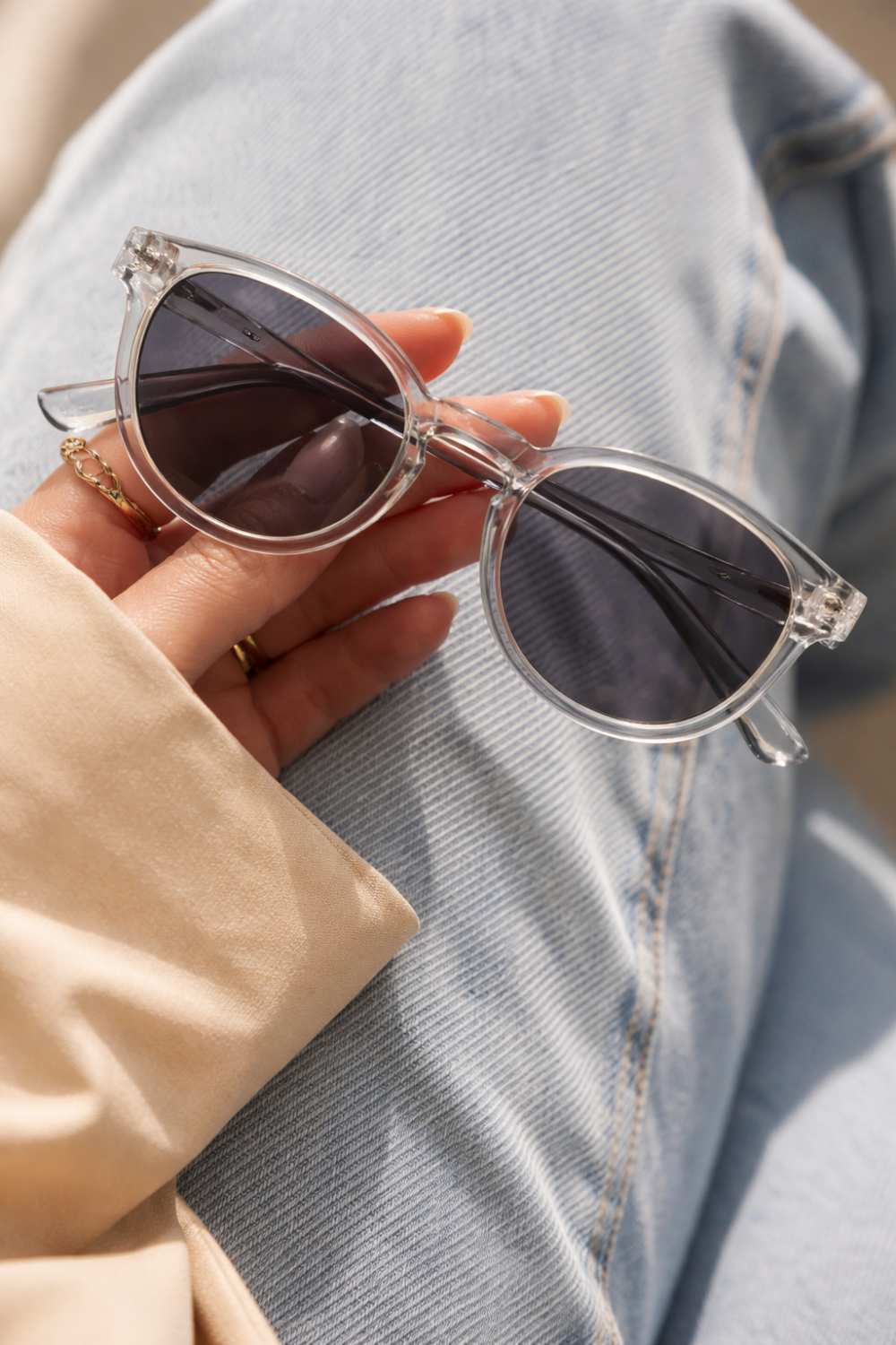 Una mano sostiene unas elegantes gafas de sol de policarbonato transparente para PC sobre un fondo de vaqueros.