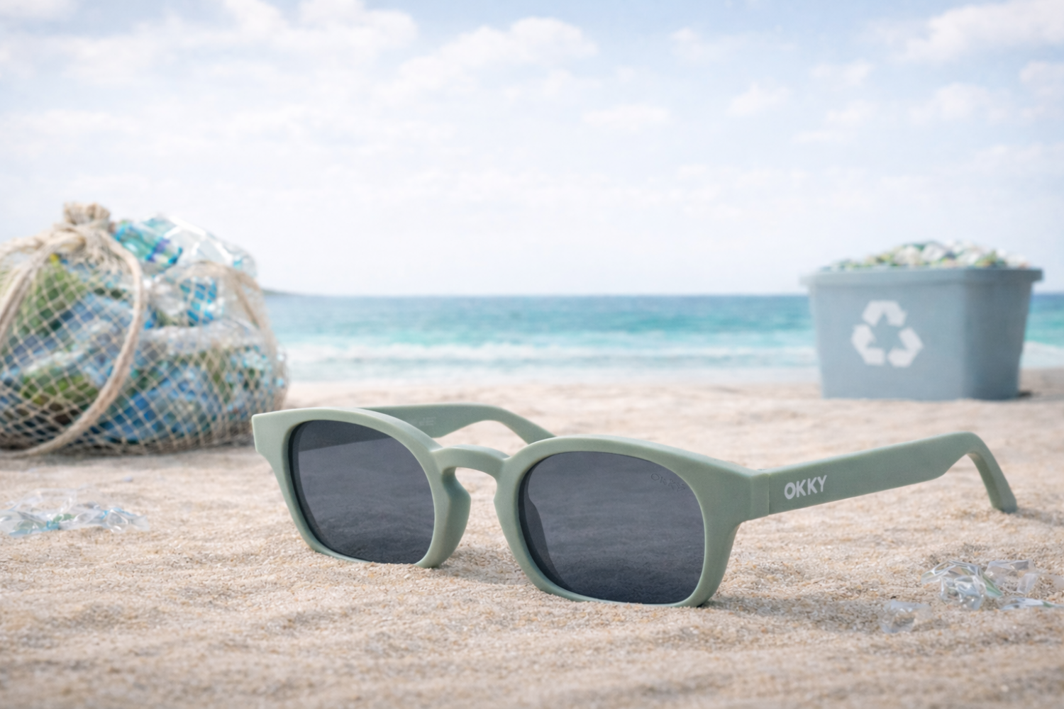 Gafas verdes sostenibles de OKKY en la playa con residuos de plástico y un contenedor de reciclaje al fondo.