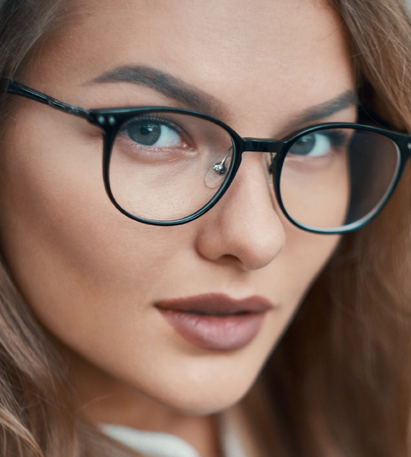 Close-up van een jonge vrouw met golvend haar en een stijlvolle zwarte bril.